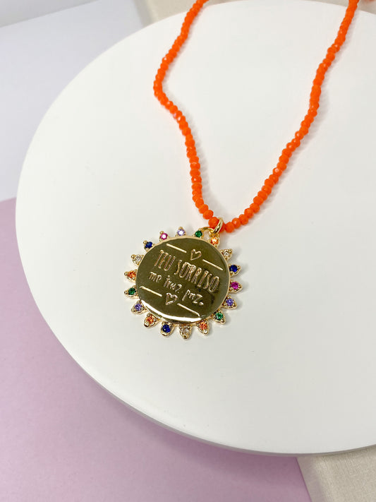 Colar cristal orange com medalha dizerem 'Teu sorriso me traz paz.'